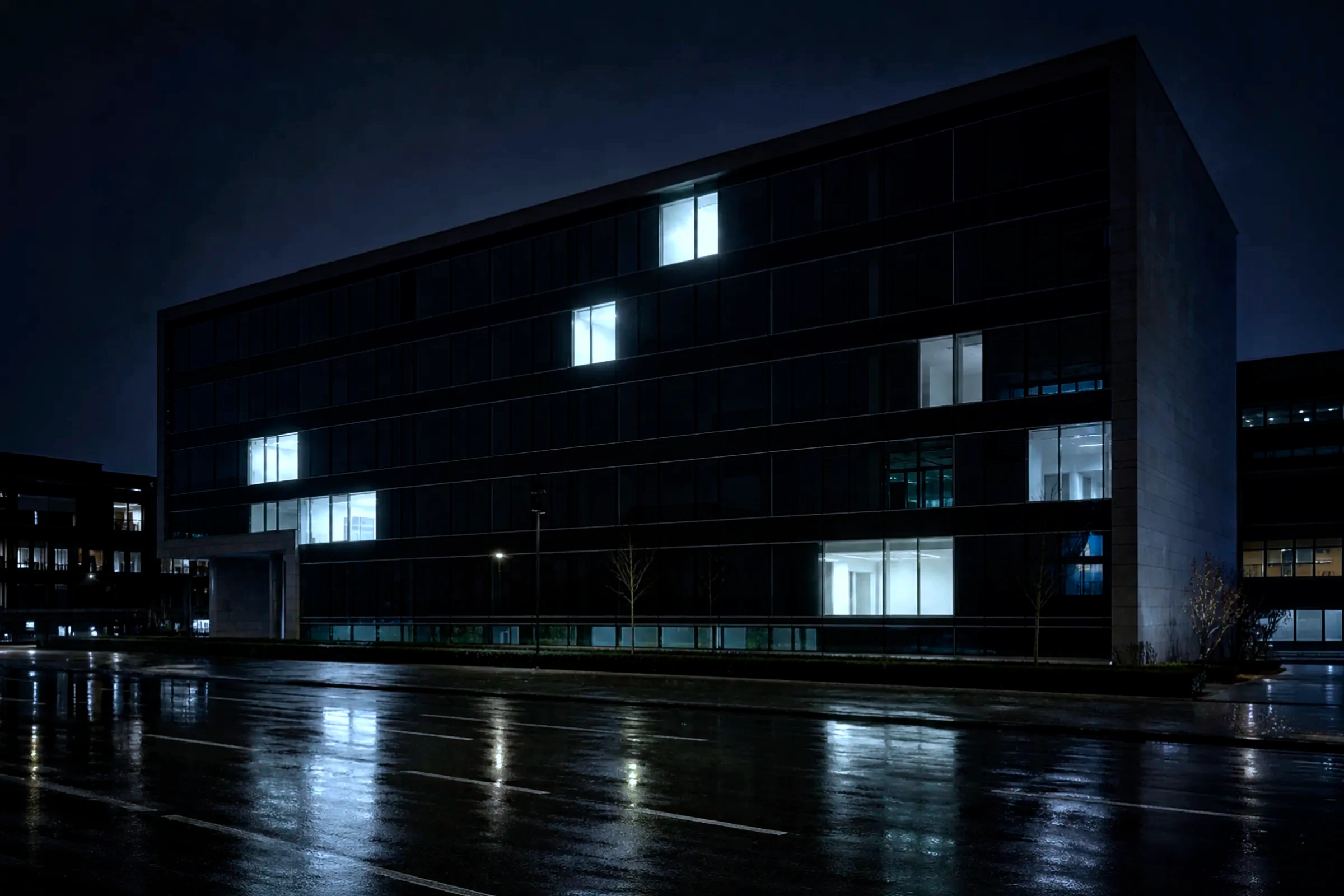 Immeuble de bureaux la nuit, facade sombre, quelques fenetres restees allumees